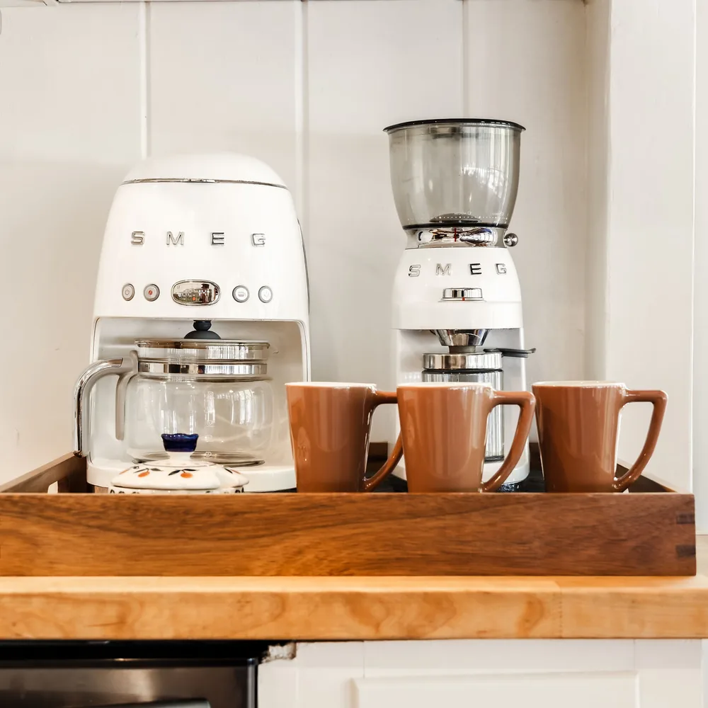 Coffee maker, grinder, and mugs on a wood tray, restocked to par for the next guest