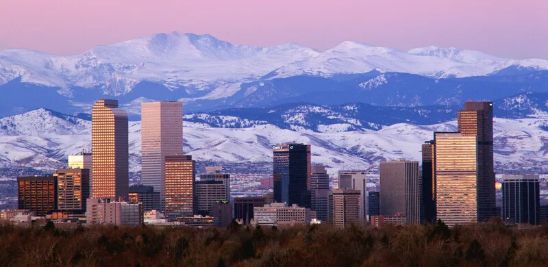 Denver skyline at golden hour with snow-capped Rocky Mountains behind